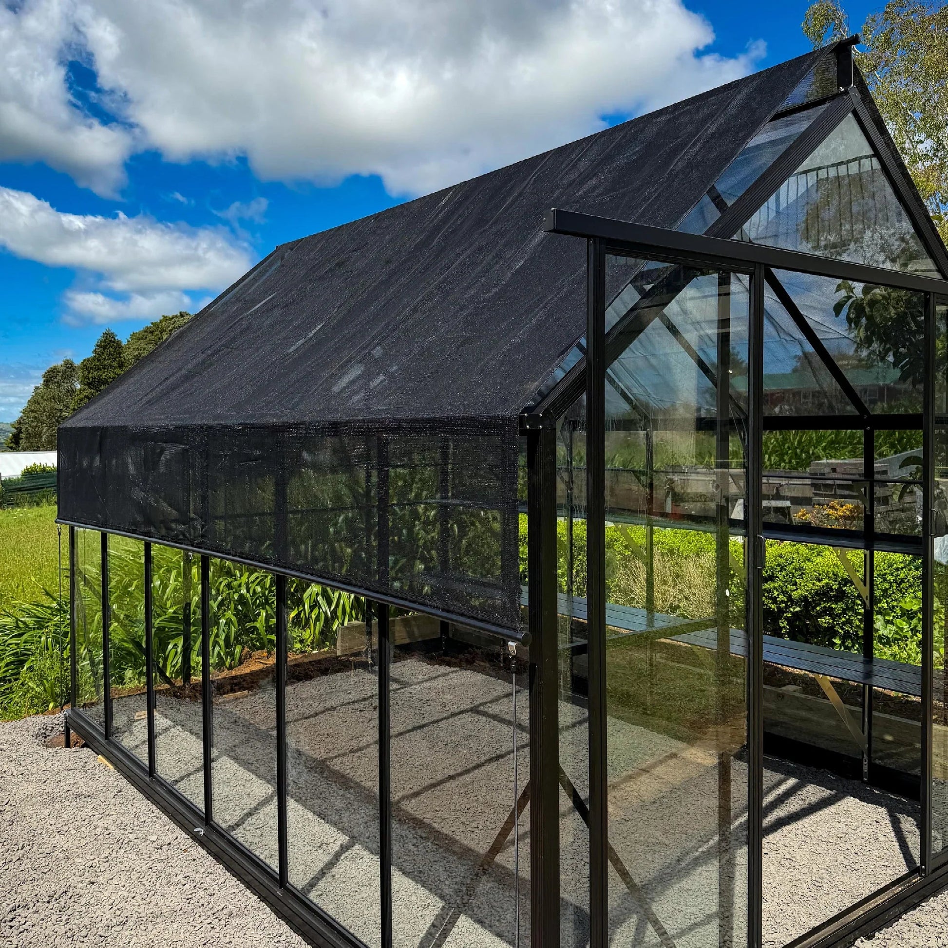 Modern glass greenhouse with black shade cover outdoors on sunny day
